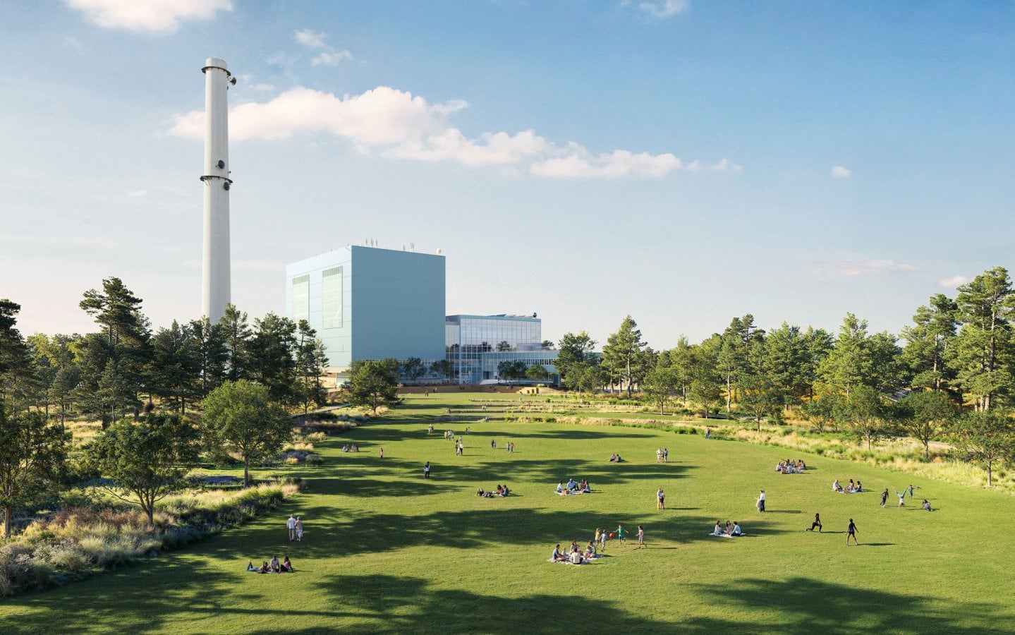 A vast green community lawn filled with people picnicking, framed by trees, with the massive blue Manresa Wilds repurposed power plant and white smokestack in the background.
