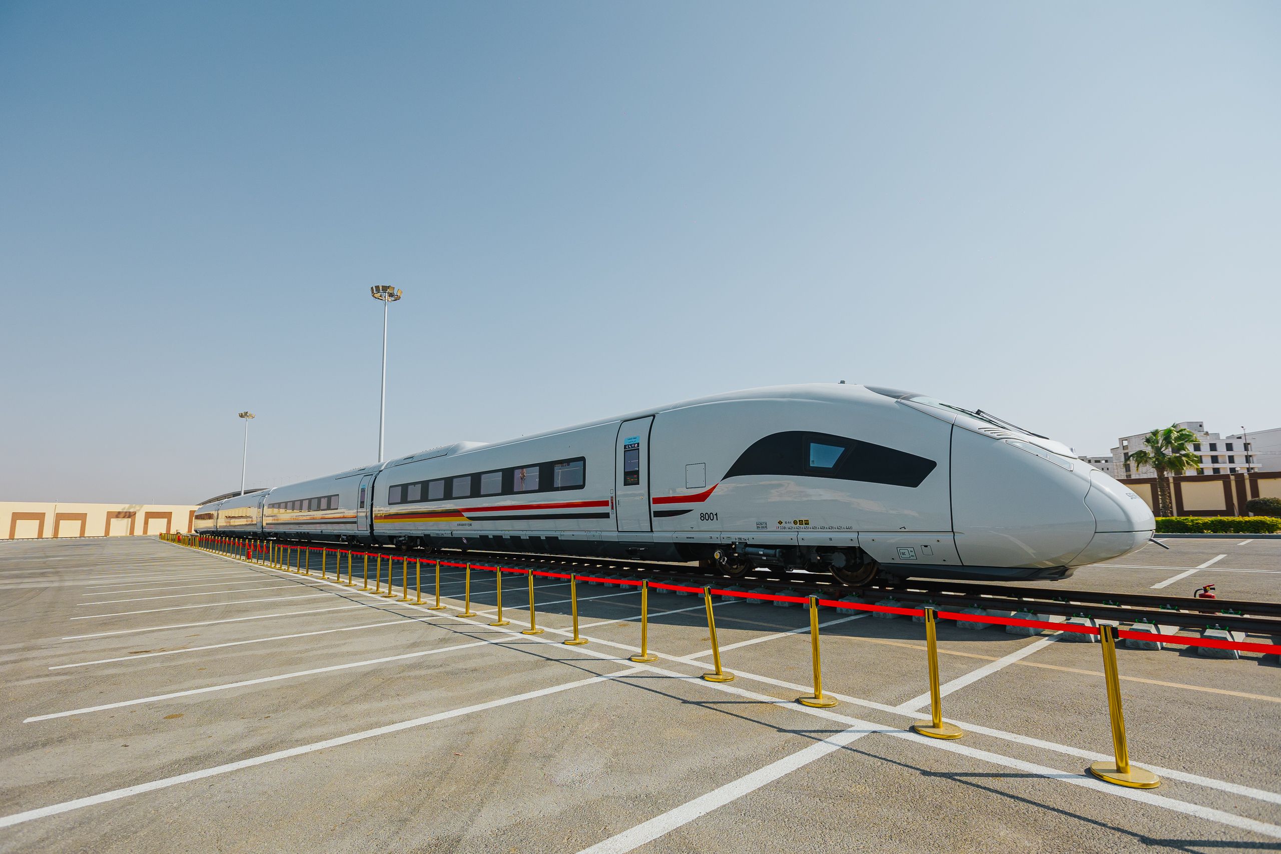 Aerial view of Egypt high-speed rail train traversing an arid desert landscape with concrete slope protection and overhead electrification masts.