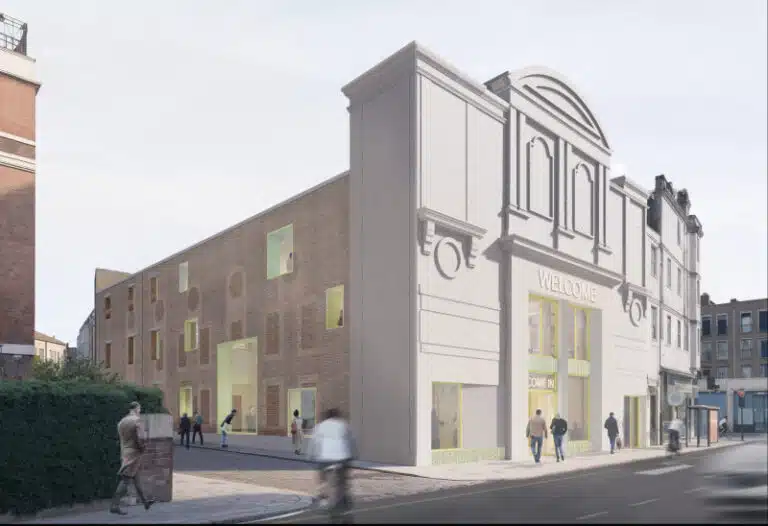 Exterior view of the Kentish Town cinema retrofit showing the preserved white Art Deco façade with a "Welcome" sign, contrasted by a new brick side elevation featuring punched windows with bright yellow frames.