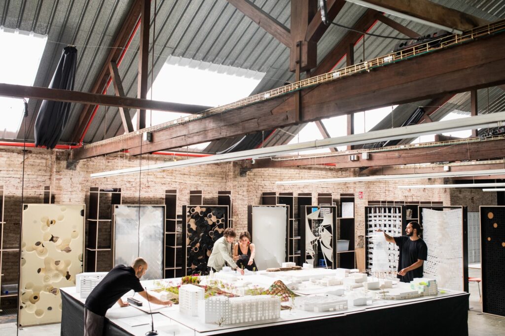 طلاب يتعاونون على نموذج خشبي كبير، مما يسلط الضوء على التعليم المعماري العملي في معهد IAAC