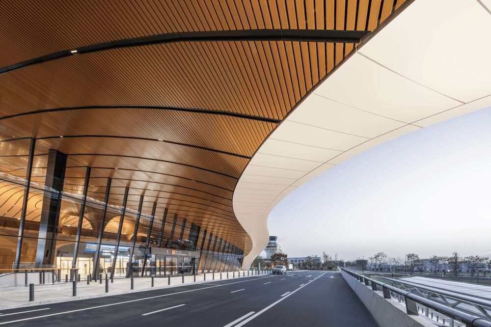 Sweeping white roof canopy with warm wood-finish ceiling slats sheltering the drop-off entrance at Lishui Airport.