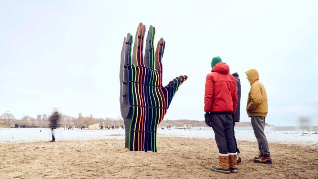 Large silhouette of a hand rising from the sand with colorful strips lining the fingers at Winter Stations.