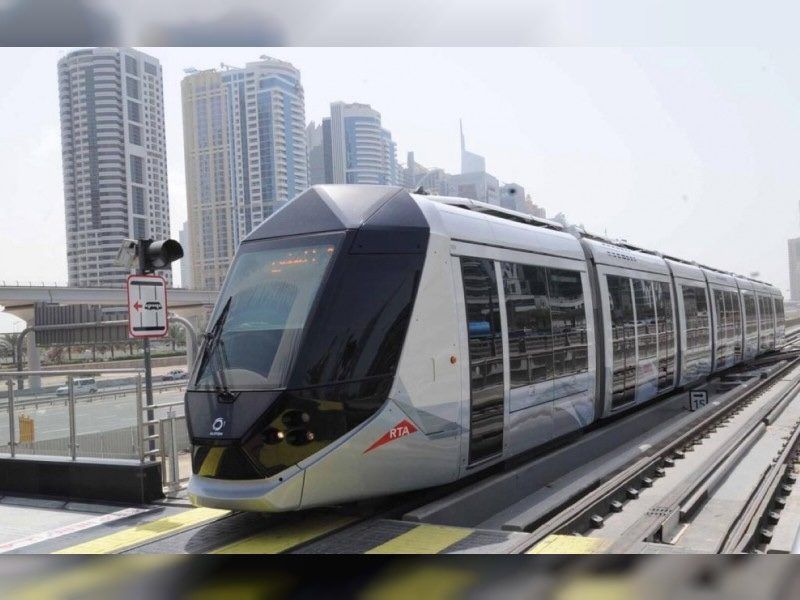 ترام فضي انسيابي يمر بجانب ناطحات السحاب الزجاجية، مما يرسخ المعيار الجمالي لأسطول الترام اللاسلكي ذاتي القيادة القادم.