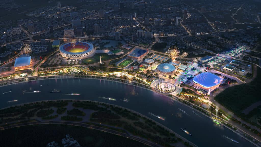 Aerial night view of the Sports District Masterplan in Ahmedabad, showing the illuminated Narendra Modi Stadium, new sports venues, and the Sabarmati Riverfront during a celebration.