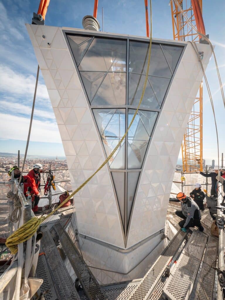 Construction workers on scaffolding installing white textured ceramic panels and glass on the peak of the Sagrada Fam&iacute;lia tower.