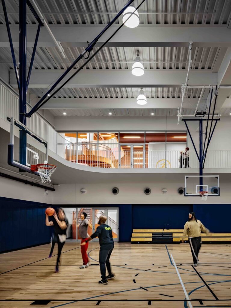 The bright and spacious gymnasium inside the Brooklyn community center, featuring a full-size basketball court with wood flooring.