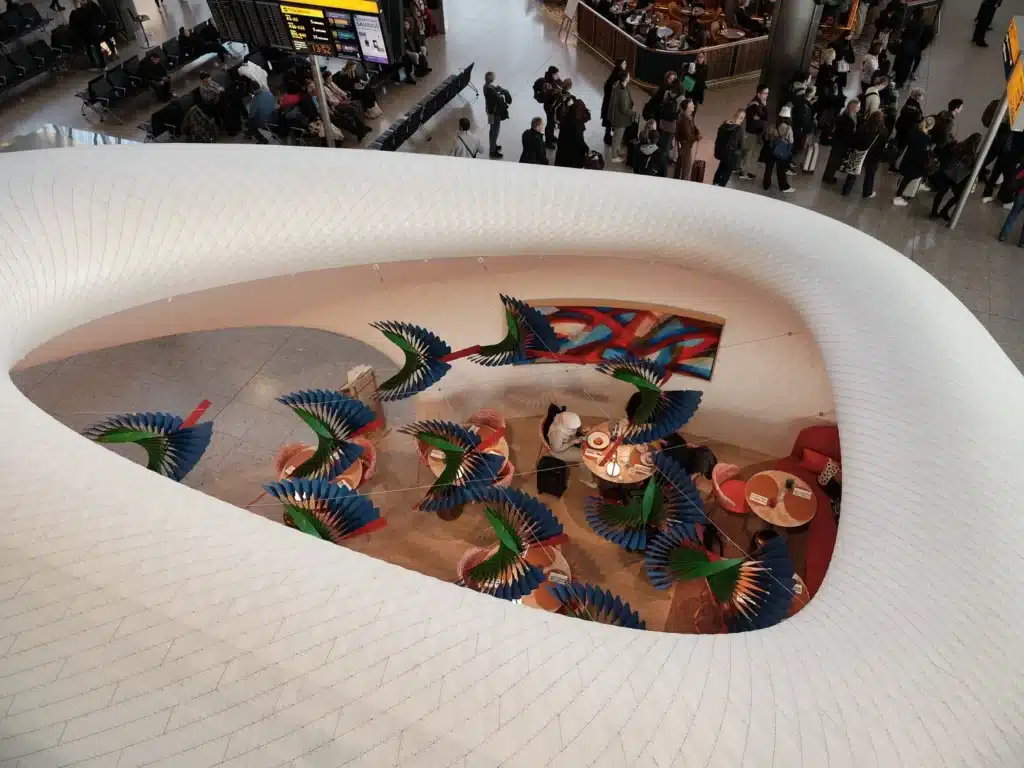 High-angle view of the cafe seating area inside the white Fuselage Architecture structure, featuring colorful suspended sculptures.