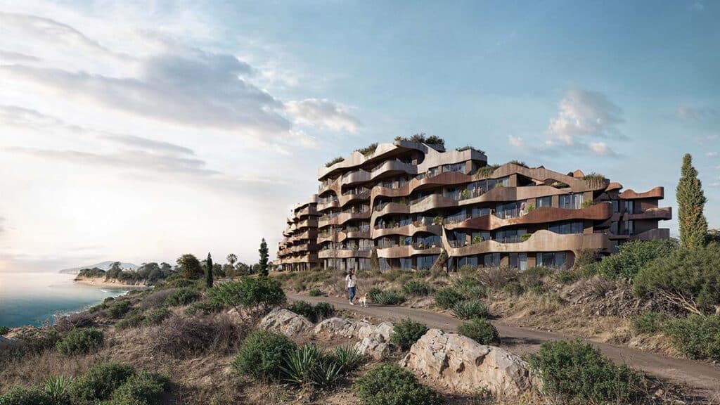 Side profile of a terraced residential complex building with organic raw plaster facades and deep balconies facing the coastline.