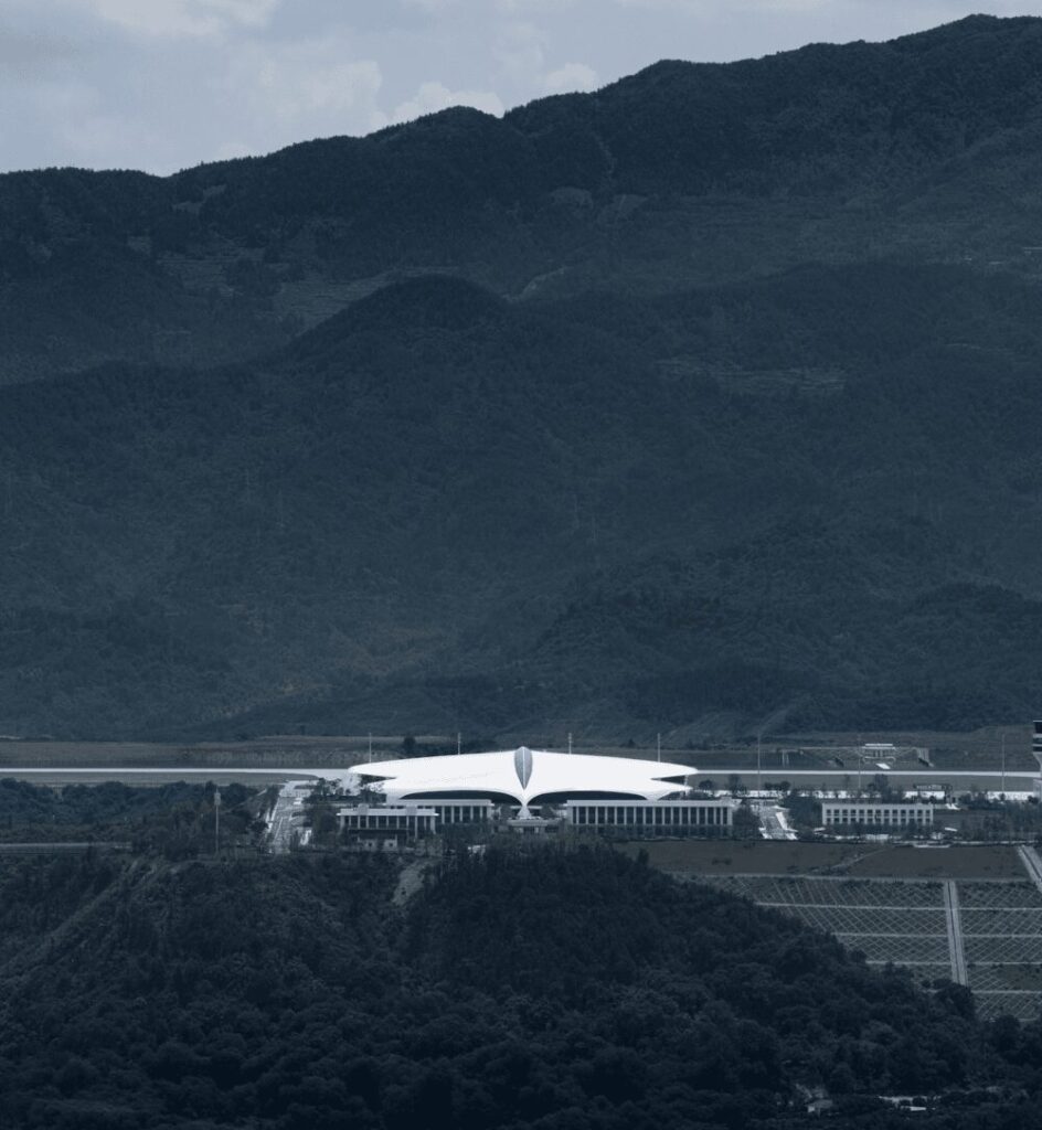 منظر بعيد لمبنى مطار ليشوي الأبيض والفتحة السقفية المركزية وهو يستقر وسط سلاسل الجبال الخضراء الداكنة.