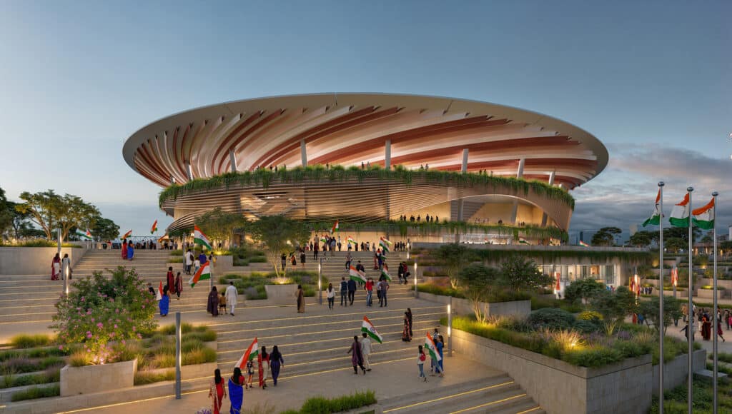 Front view of a circular sports venue with bronze-colored louvered screens and terraced landscaping, a key element of the Sports District Masterplan.