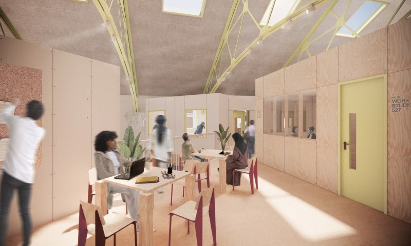 Upper-level co-working space in the cinema retrofit with exposed yellow steel roof trusses, plywood partition walls, and natural light filtering through overhead skylights.