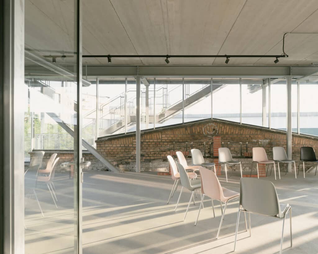 A wide exterior shot of the ZK/U Center at dusk, illustrating the transparent quality of the new addition in this architectural reuse project.