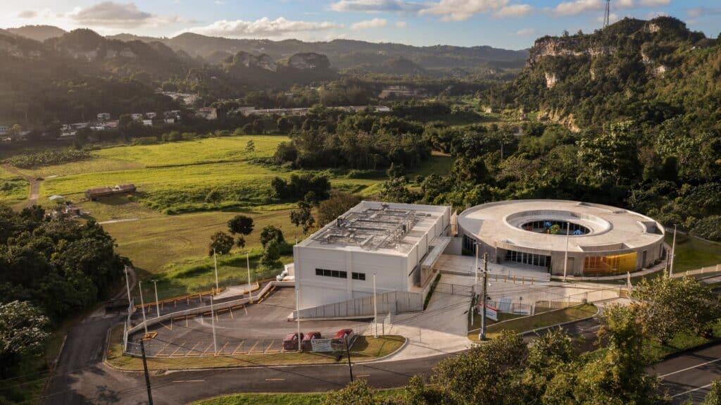 Aerial view of the circular school situated next to the white administrative building against karst cliffs.