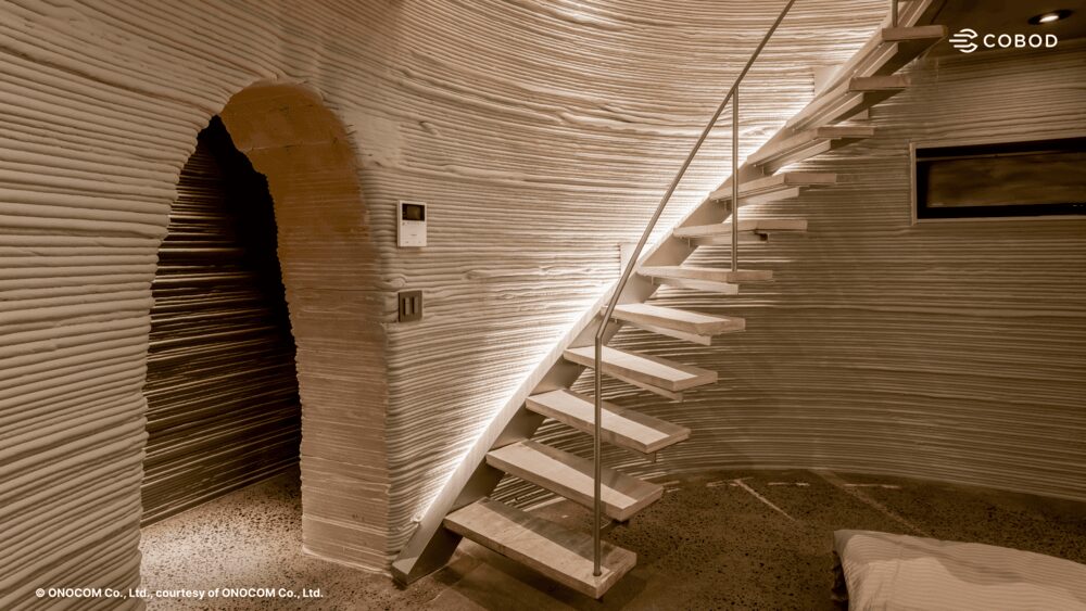 Detailed view of a curved wooden staircase and arched passageway illustrating the structural geometry of the 3D-printed house.