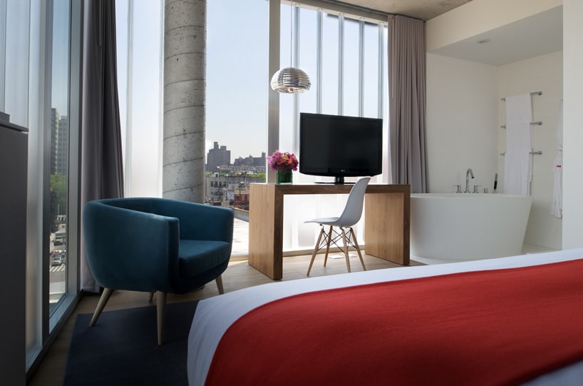 Interior view of a modern furnished apartment room with floor-to-ceiling windows looking out onto a balcony.