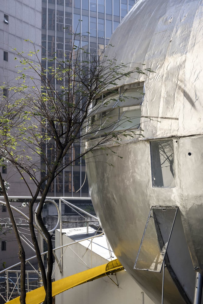 Close-up detail of the ferrocement facade and louvered windows of the Spherical House against a modern glass skyscraper.