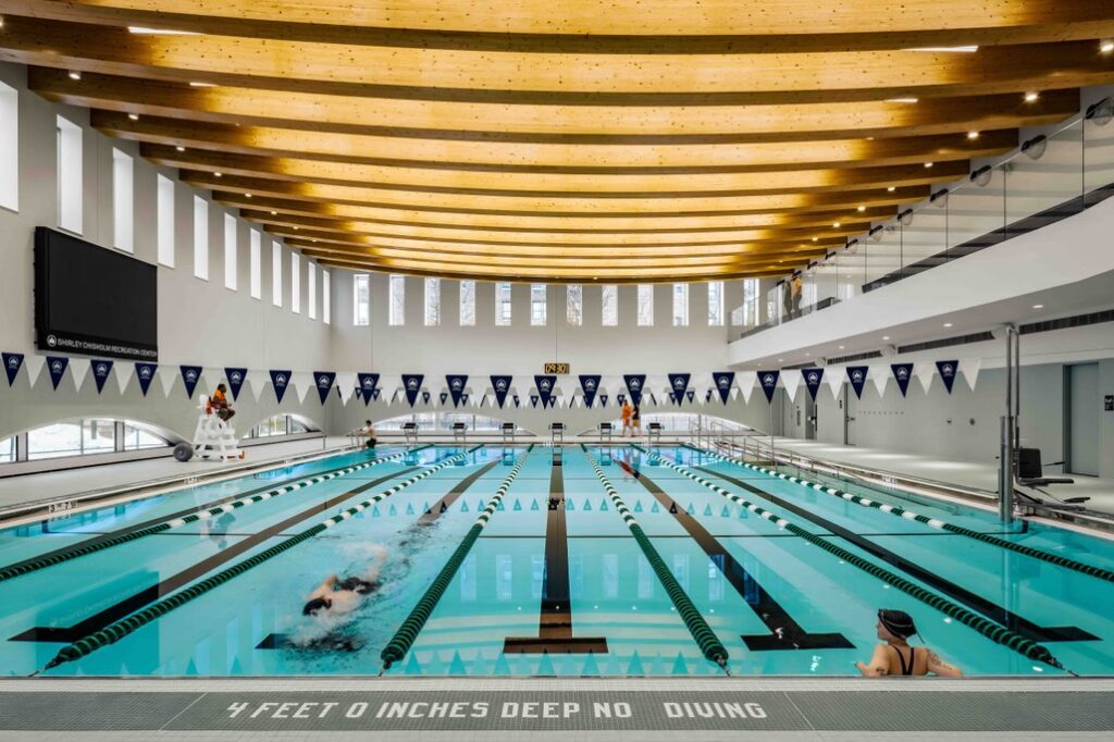 The double-height, competition-grade swimming pool inside the new community center, with mass timber beams spanning the ceiling.