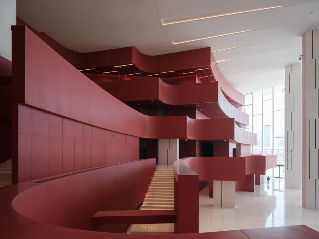 Interior view of the Shanghai Grand Opera House featuring deep red curvilinear balconies and a white polished floor.