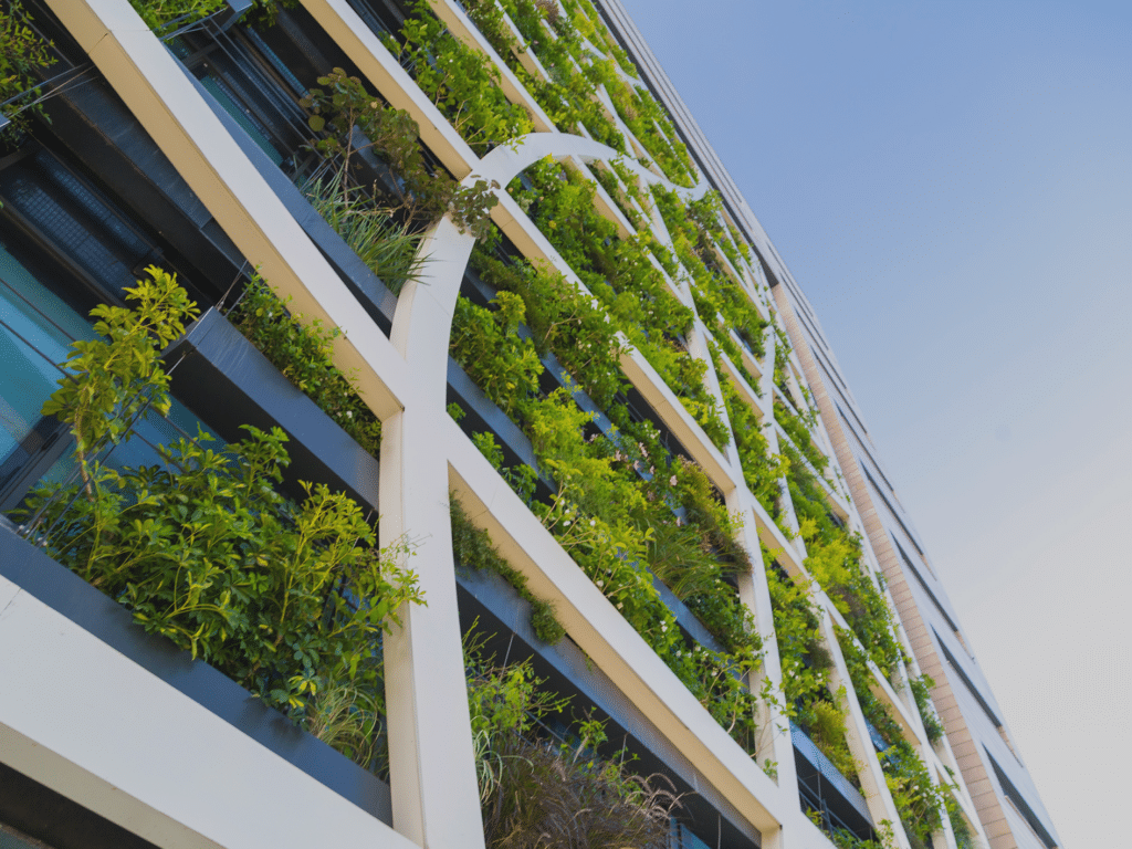 A low-angle shot of a modern white building facade covered in lush green plants and vertical gardens integrated into its balconies.