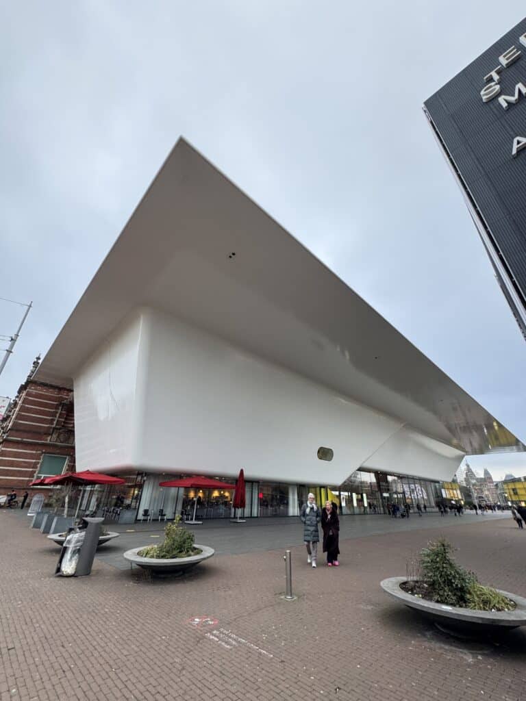 A spacious, multi-level modern museum atrium featuring a translucent glass ceiling, minimalist white walls, and visitors exploring the interior spaces.