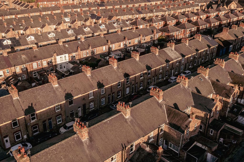 High-angle aerial view of long rows of red-brick terraced houses with slate roofs and chimney pots under warm evening sunlight.
