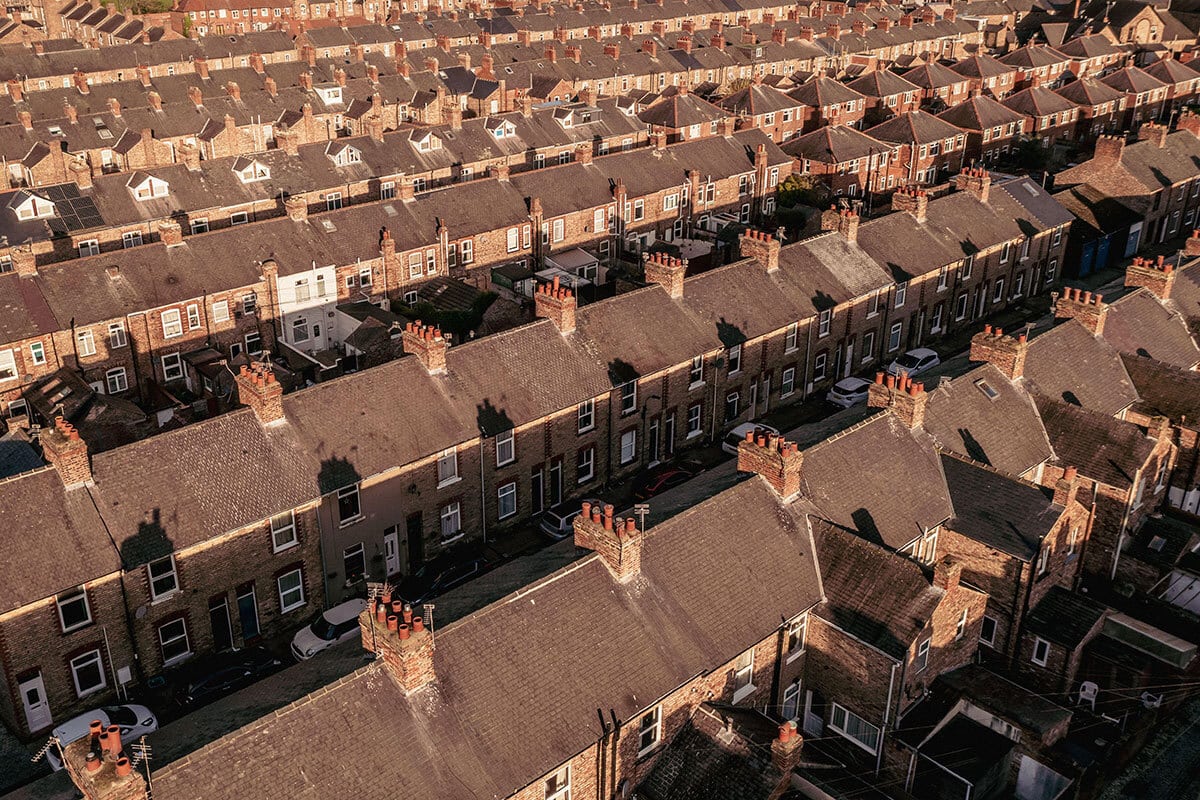 High-angle aerial view of long rows of red-brick terraced houses with slate roofs and chimney pots under warm evening sunlight.