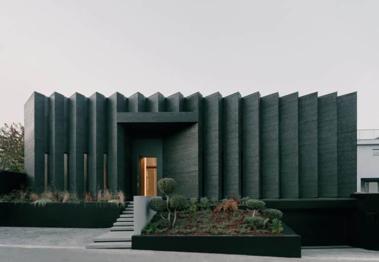 Front view of Okrokana residence in Tbilisi showing the charred wood facade with vertical rhythmic patterns and a landscaped entrance.