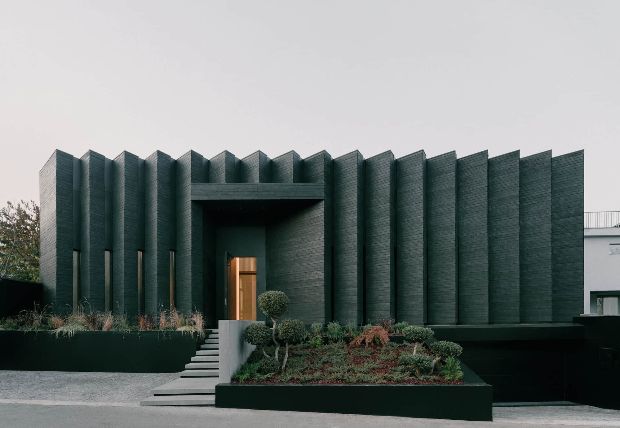 Front view of Okrokana residence in Tbilisi showing the charred wood facade with vertical rhythmic patterns and a landscaped entrance.