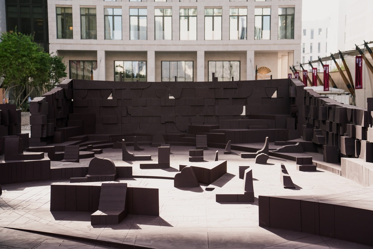 A wide interior view of the architectural installation "In the Assembly of Loved Ones" by Counterspace, featuring dark brown modular wooden elements arranged in a communal gathering space.