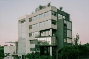 A contemporary office building rehabilitation showing a multi-textured facade with glass panels, grey concrete walls, and a rooftop garden under a clear sky.