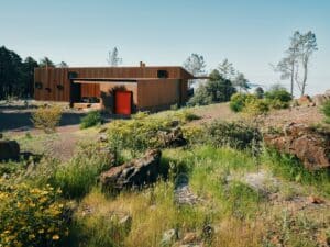 Exterior view of Healdsburg house featuring fire-resistant weathered steel cladding and a bright red garage door in a mountainous landscape.