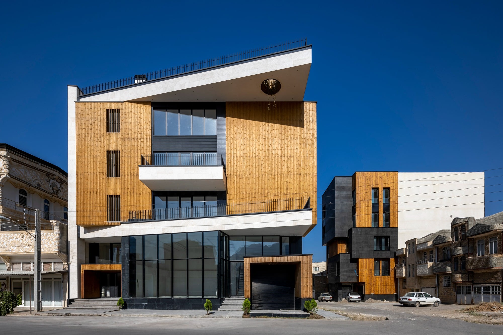 Front elevation of Ramand Ho building featuring a wooden-clad cube and white geometric lines at a street corner.