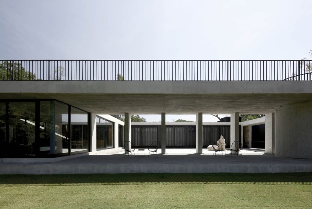 A wide view of a concrete colonnade and a covered terrace overlooking a green lawn under a bright sky.