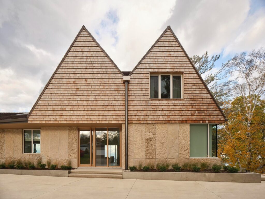 Front facade of a modern Georgian Bay house featuring symmetrical twin gables, cedar shingle roofing, and local limestone walls.