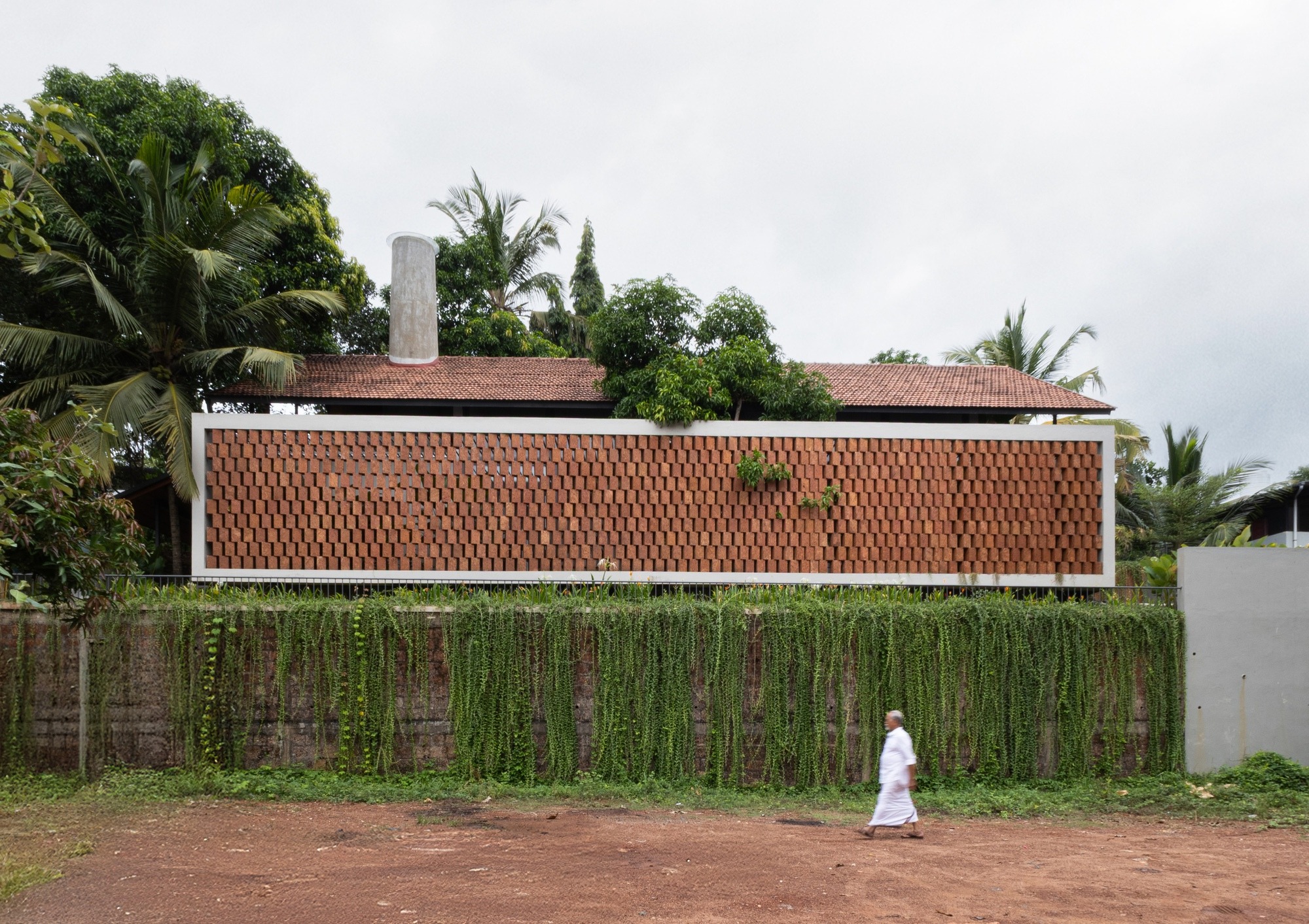 Front elevation of a modern house featuring a long laterite stone jaali wall and a lush green creeper-covered retaining wall.