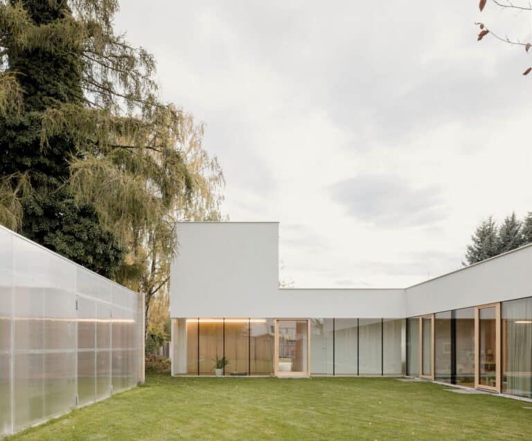 Exterior view of the contemporary Sestajovice House in Prague featuring white L-shaped minimalist architecture and a wide green lawn.
