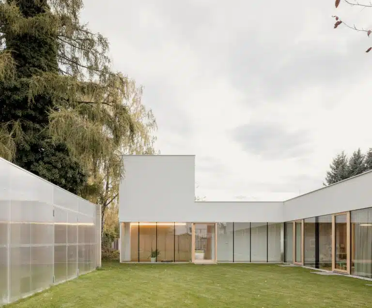 Exterior view of the contemporary Sestajovice House in Prague featuring white L-shaped minimalist architecture and a wide green lawn.