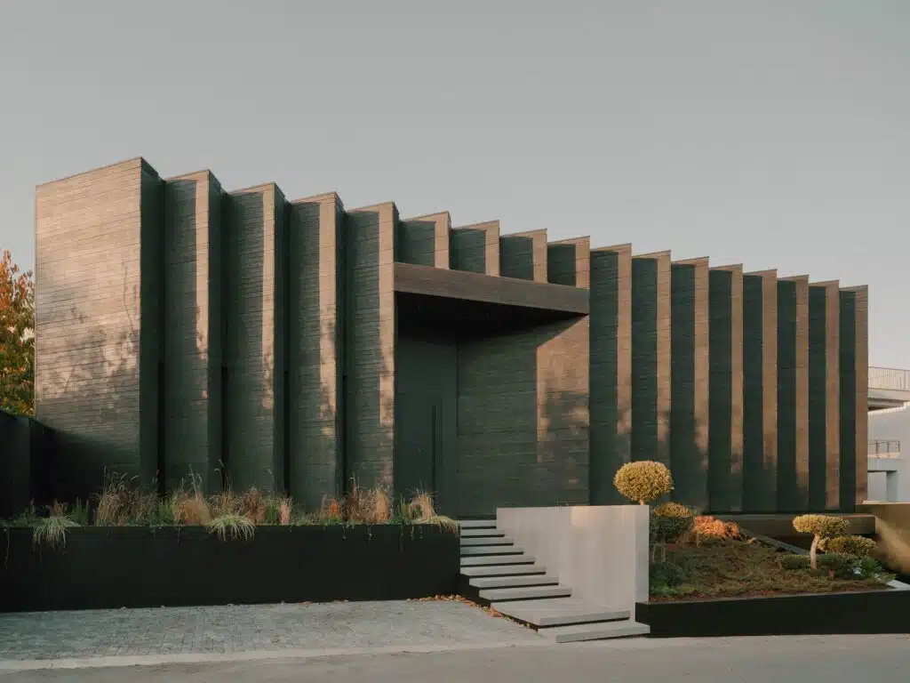 Side angle of the Okrokana house exterior showing the jagged edge of the charred wood facade under soft sunlight.