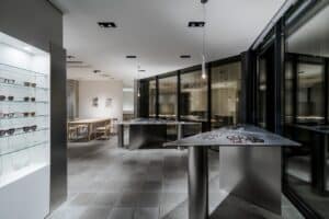 Interior view of Ashiya Optical Store showing triangular display tables and a curved glass facade overlooking the city.