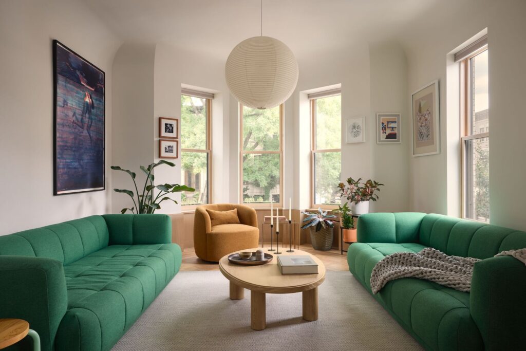 A bright living room with two green modular sofas, a light wood coffee table, and soft curved ceiling edges.