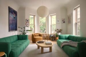 A bright living room with two green modular sofas, a light wood coffee table, and soft curved ceiling edges.