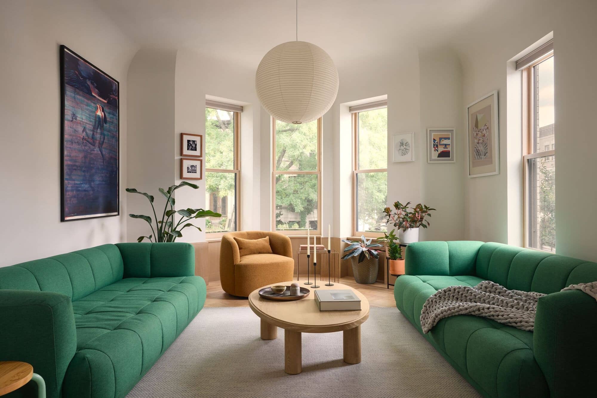 A bright living room with two green modular sofas, a light wood coffee table, and soft curved ceiling edges.