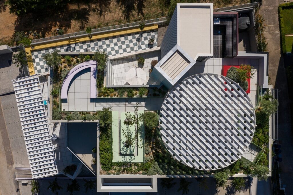 High-angle aerial view of a sustainable office rooftop featuring geometric landscaping, circular shading structures, and vibrant outdoor furniture.