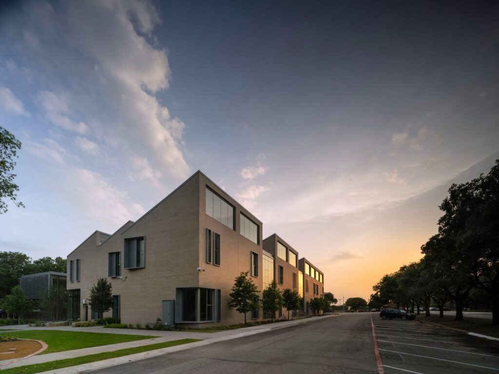 Exterior view of the brick building at Greenhill School during sunset, showing the modular classroom wings and parking area.
