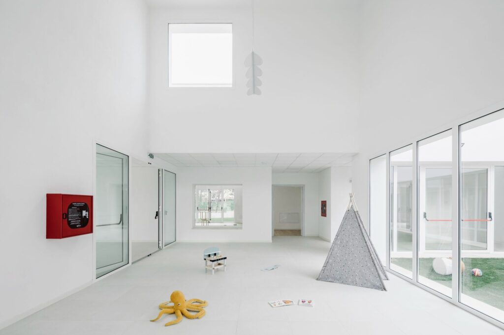 High-ceiling interior play area with white walls, natural light, and a small play tent.