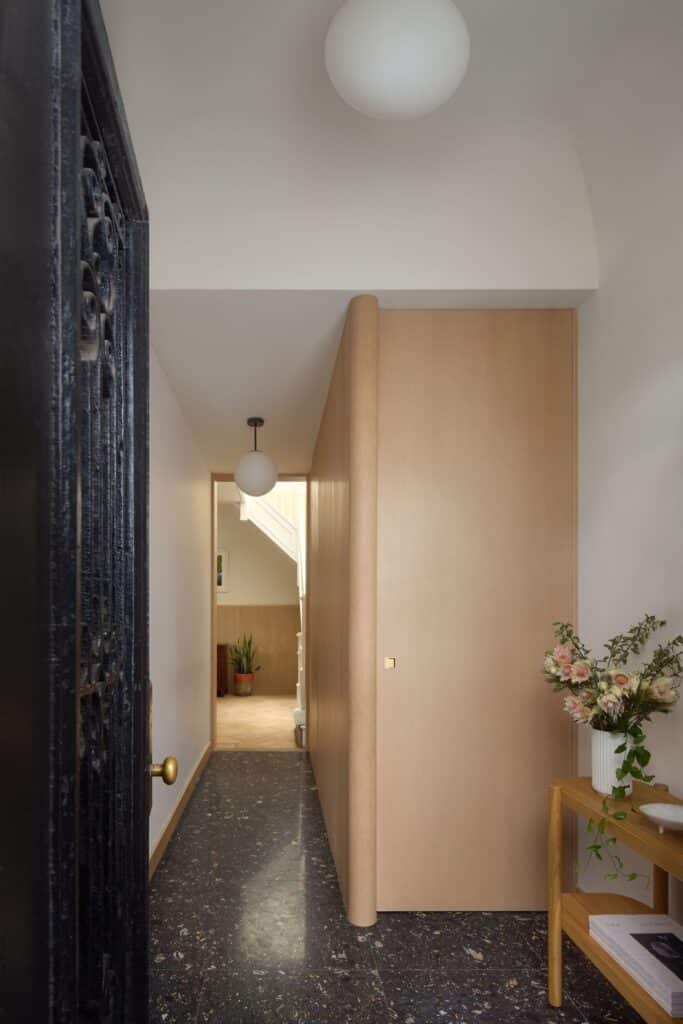 A modern entryway featuring dark terrazzo flooring, light wood storage cabinets, and minimalist globe lighting.