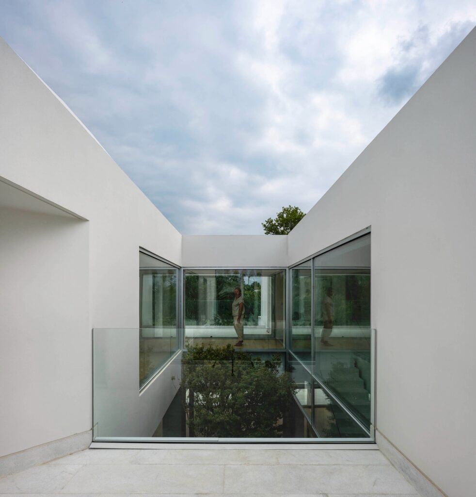 Looking down into a glass-walled internal courtyard of a white villa under a cloudy sky.