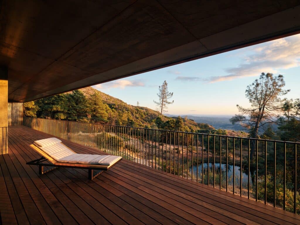 Sunset view from a wooden cantilevered deck with a lounge chair overlooking a valley and a natural retention pond.