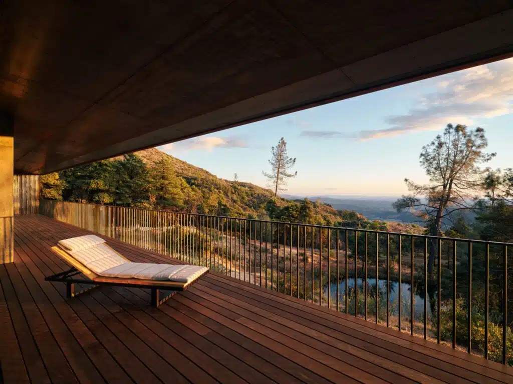 Sunset view from a wooden cantilevered deck with a lounge chair overlooking a valley and a natural retention pond.