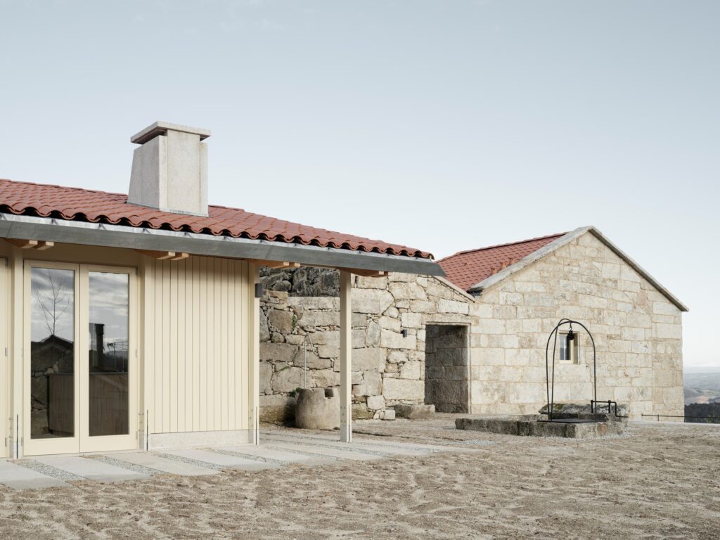 Exterior detail of the rehabilitated stone building and the new pavilion entrance, featuring a traditional stone well in the foreground.